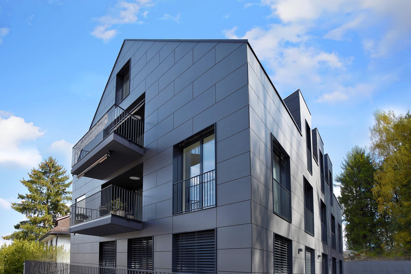 Moderner Neubau mit dunkler Fassade und Balkonen vor blauem Himmel